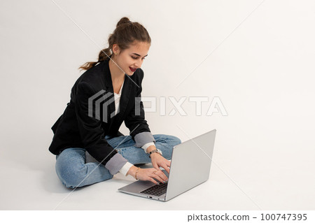 the girl is sitting on the floor and working or communicating on a laptop. the girl is sitting on the floor and working or communicating on a laptop. 100747395
