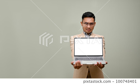 Determined Asian businessman holds a laptop mockup, stands against an isolated background 100748401