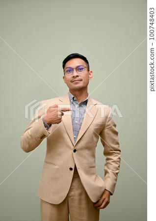 Handsome millennial Asian businessman pointing finger aside, hand in pocket 100748403