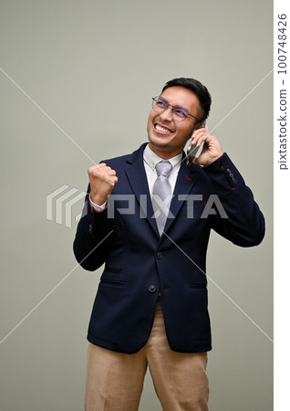 Successful Asian businessman on the phone, showing YES gesture, celebrating his success Successful Asian businessman on the phone, showing YES gesture, celebrating his success 100748426