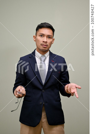Angry and unhappy millennial Asian businessman opening his palm, and looking at the camera Angry and unhappy millennial Asian businessman opening his palm, and looking at the camera 100748427