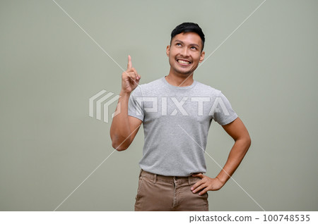 Cheerful Asian man looking up and pointing his finger up at the empty space 100748535