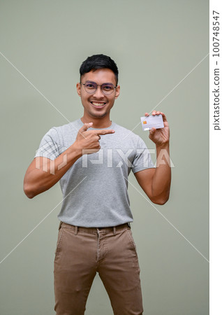 Smiling Asian man pointing his finger to a credit card on his hand. isolated background 100748547