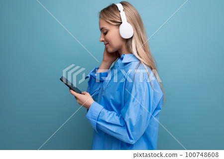 bright cute girl in wireless large headphones with a phone in her hands listens with pleasure to 100748608
