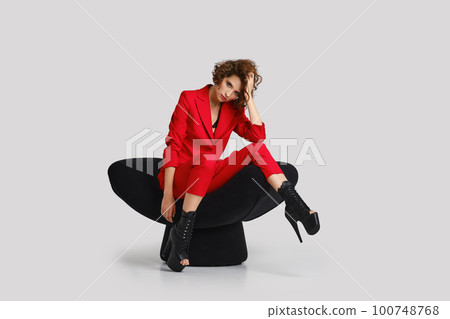 Tired young woman in red pantsuit sits in armchair 100748768