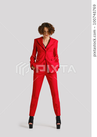 Angry woman stands with hands in pockets of her red jacket 100748769