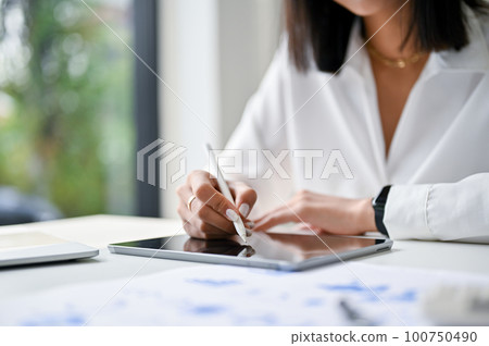 Cropped image of a businesswoman or female boss using her tablet in the financial meeting. Cropped image of a businesswoman or female boss using her tablet in the financial meeting. 100750490