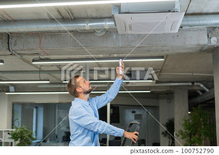 Caucasian bearded man repairing the air conditioner in the office. Caucasian bearded man repairing the air conditioner in the office. 100752790