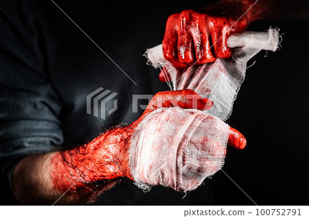 A man covered in blood bandages his hands. 100752791