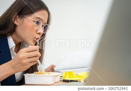 Busy and tired businesswoman eating spaghetti for lunch at the Desk office and working to deliver financial statements to a boss. Overworked and unhealthy for ready meals, burnout concept. Busy and tired businesswoman eating spaghetti for lunch at the Desk office and working to deliver financial statements to a boss. Overworked and unhealthy for ready meals, burnout concept. 100752941