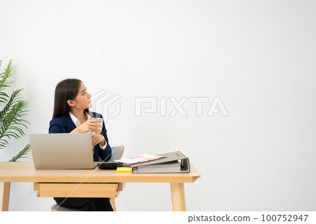 Young pensive businesswoman at desk with laptop dreamful for successful and holding milk glass  isolated on white background. 100752947