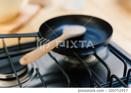 Spatula in skillet teflon coating pan on gas stove against spoon hanging in small kitchen 100752957