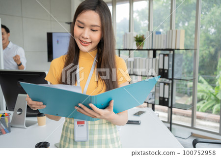 Young Asian Happy Businesswoman or intern holding documents in Modern Office background is Colleagues discuss with new startup project Idea. Empowered Digital Entrepreneur Works on Startup Project 100752958