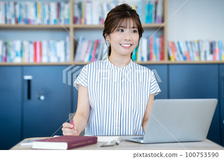 Young woman using a laptop in the library 100753590