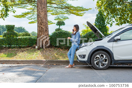 Angry Asian woman and using mobile phone calling for assistance after a car breakdown on street. Concept of vehicle engine problem or accident and emergency help from Professional mechanic 100753736