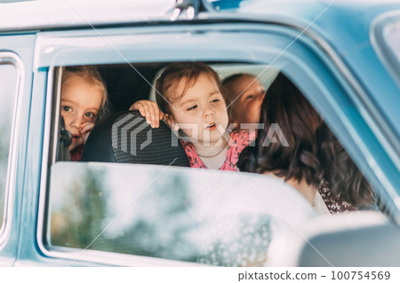 Cheerful little sisters sitting in blue car and feeling happy for an exciting family trip outside 100754569
