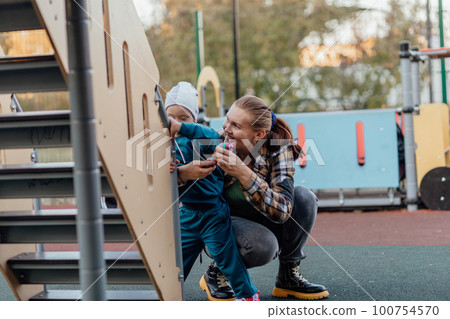 The mother of a little boy with Down syndrome keeps him from trying to climb the stairs on the playground, the concept of safety 100754570