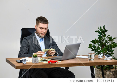 young bearded businessman working on laptop and holding money 100754613