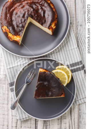 Sliced tender creamy burnt basque cheesecake with lemon wedges close-up on a plate. Vertical top view Sliced tender creamy burnt basque cheesecake with lemon wedges close-up on a plate. Vertical top view 100756073