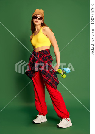 Full-length photo of young skateboarding girl wearing stylish clothes and holding skateboard in hands over green background Full-length photo of young skateboarding girl wearing stylish clothes and holding skateboard in hands over green background 100756768