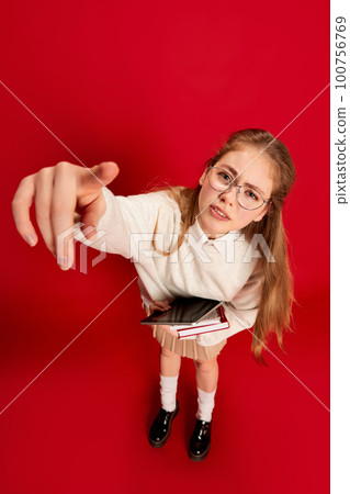 Photo of disappointed student girl wearing glasses, holding tablet, and pointed with finger at camera over red background. Top view Photo of disappointed student girl wearing glasses, holding tablet, and pointed with finger at camera over red background. Top view 100756769