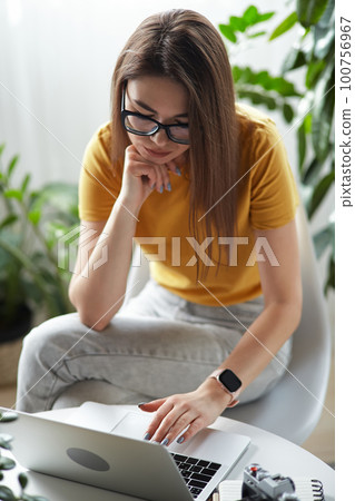 Young woman designer or freelancer working at home using computer sitting at table at home Young woman designer or freelancer working at home using computer sitting at table at home 100756967
