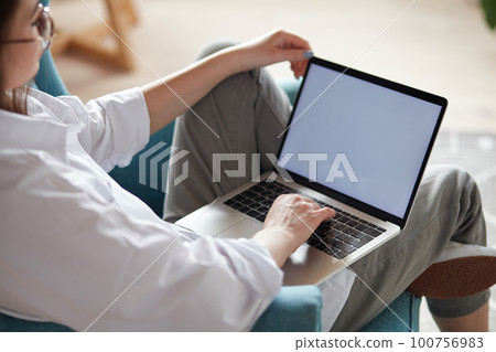 Mockup white screen laptop woman using computer sitting on armchair at home, back view, focus on screen 100756983
