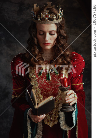 medieval queen in red dress with book, candle and crown 100757166