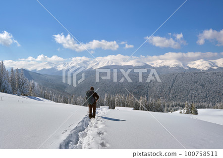 Man backpacker hiking snowy mountain hillside on cold winter day. Man backpacker hiking snowy mountain hillside on cold winter day. 100758511