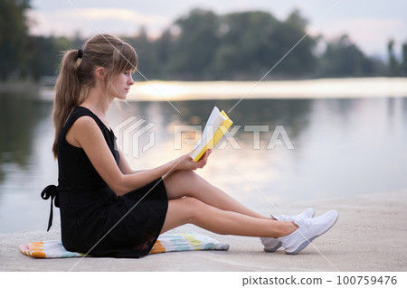 Female student sitting in summer park reading textbook outdoors. Education and sudy concept. Female student sitting in summer park reading textbook outdoors. Education and sudy concept. 100759476