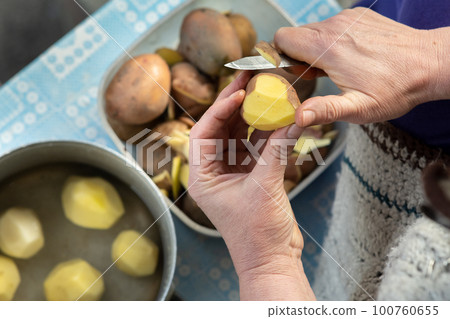 Closeup of woman hands peeling potatoes with a kitchen knife. 100760655