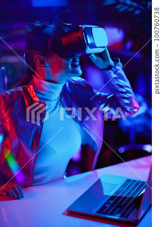 curious stylish female in virtual reality goggles in office 100760738
