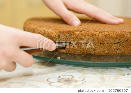 Closeup of female hand holding sharp knife cutting biscuit chocolate cake. Working process of homemade baking. 100760807