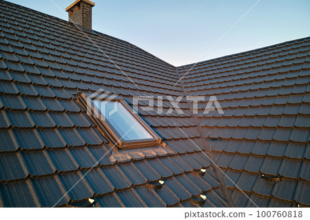 Closeup of attic window on house roof top covered with ceramic shingles. Tiled covering of building 100760818