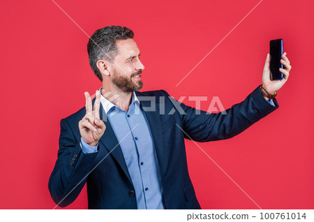 happy businessman making selfie. male business blogger. vlogger with cellphone show peace gesture. 100761014