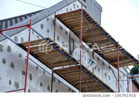 Building facade under renovation works with construction scaffolding frame. Wall insulation with styrofoam sheets for energy efficient home Building facade under renovation works with construction scaffolding frame. Wall insulation with styrofoam sheets for energy efficient home 100761918
