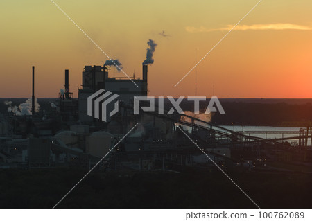 Aerial view of wood processing factory with smoke from production process polluting atmosphere at plant manufacturing yard. Industrial site at sunset Aerial view of wood processing factory with smoke from production process polluting atmosphere at plant manufacturing yard. Industrial site at sunset 100762089
