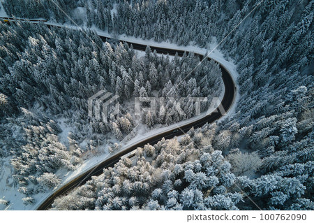 Aerial view of winter landscape with snow covered mountain hills and winding forest road in morning. 100762090