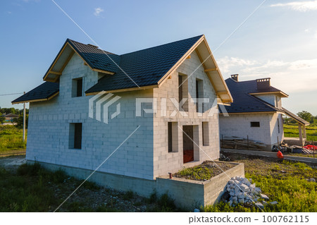 Aerial view of unfinished house with aerated lightweight concrete walls and wooden roof frame covered with metallic tiles under construction 100762115