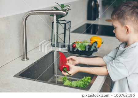 Six-year-old boy washing vegetables in the kitchen sink. Side view. 100762190