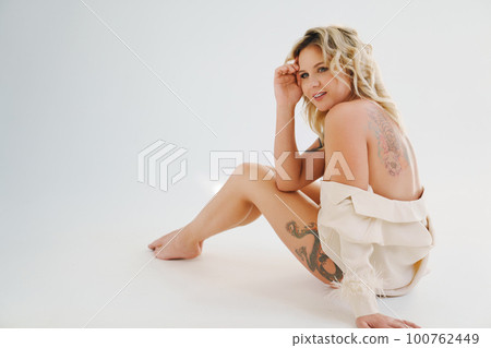 a gentle naked blonde woman in a white shirt on the floor.  100762449