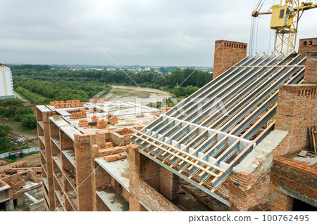 Aerial view of unfinished brick apartment building with wooden roof structure under construction. 100762495