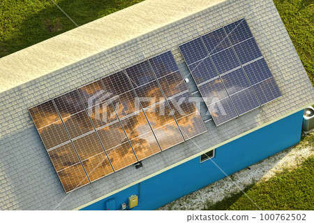 Aerial view of typical american building roof with rows of blue solar photovoltaic panels for producing clean ecological electric energy. Renewable electricity with zero emission concept Aerial view of typical american building roof with rows of blue solar photovoltaic panels for producing clean ecological electric energy. Renewable electricity with zero emission concept 100762502