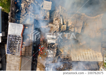 Aerial view of ruined building on fire with collapsed roof and rising dark smoke. Aerial view of ruined building on fire with collapsed roof and rising dark smoke. 100762675