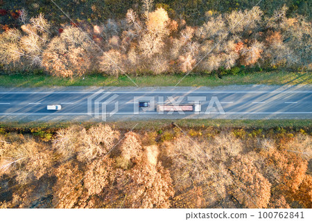 Aerial view of intercity road with fast driving cars between autumn forest trees at sunset. Top view from drone of highway traffic in evening 100762841