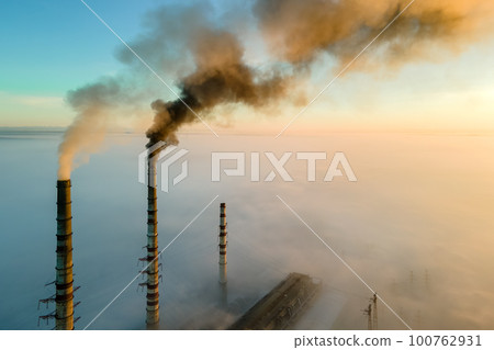 Aerial view of coal power plant high pipes with black smoke moving up polluting atmosphere at sunrise. 100762931