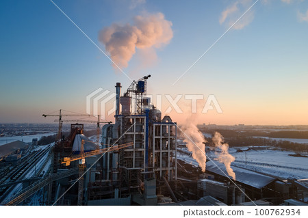 Aerial view of cement factory with high concrete plant structure and tower cranes at industrial production area. Greenhouse gas smoke polluting atmosphere. Manufacture and global industry concept. Aerial view of cement factory with high concrete plant structure and tower cranes at industrial production area. Greenhouse gas smoke polluting atmosphere. Manufacture and global industry concept. 100762934