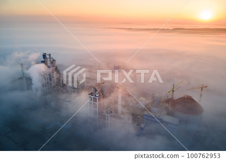 Aerial view of cement factory with high concrete plant structure and tower crane at industrial manufacturing site on foggy evening. Production and global industry concept. 100762953