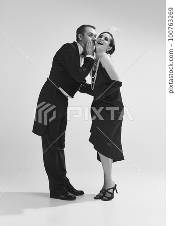 Studio shot of couple wearing old-time evening costume and talking with smiling faces. Monochrome 100763269