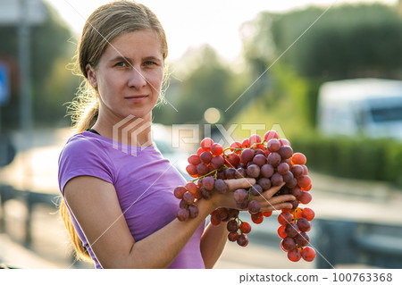 A woman holding big cluster of red juicy grapes in her hand. A woman holding big cluster of red juicy grapes in her hand. 100763368